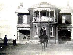 Jeune homme à cheval devant une grande maison en briques